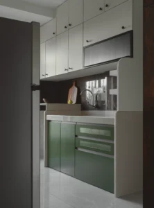 Two-tone modular kitchen with cream upper cabinets, sage green lower cabinets with perforated drawer fronts, a dark stone backsplash, and a chrome gooseneck faucet in a contemporary Indian apartment.