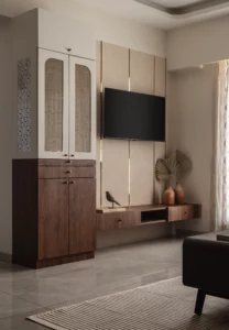 Living room TV wall featuring a warm beige textured panel with vertical brass strips, a floating walnut media console with terracotta vases, and a full-height white storage cabinet with arched cane-panelled doors.